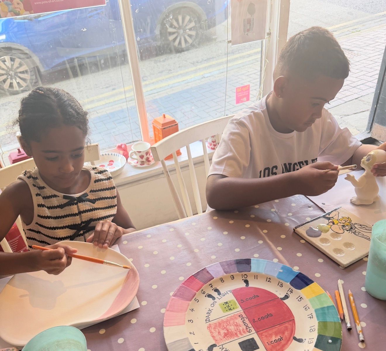 Two children painting clay figures at a kitchen table